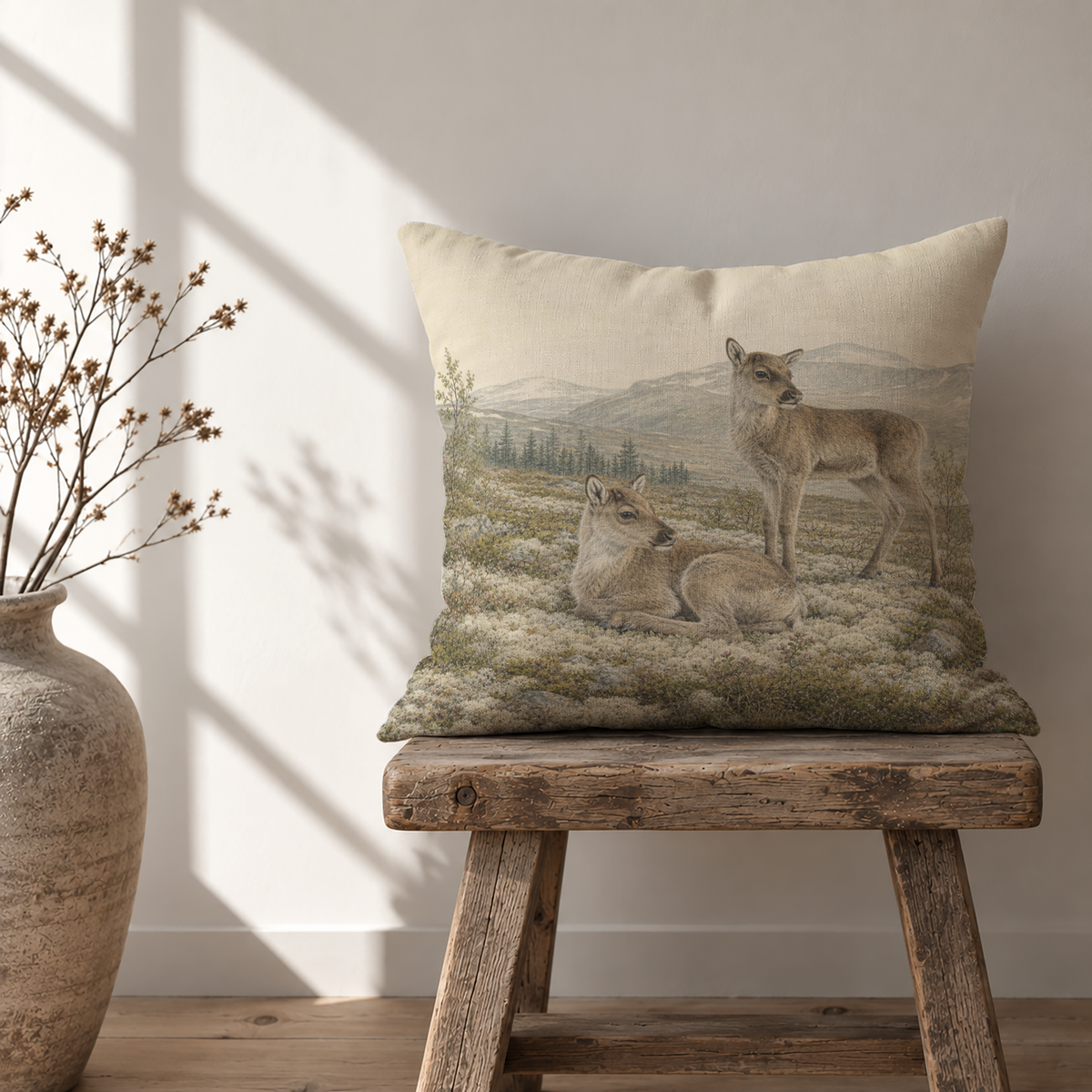 Rustic reindeer calf pillow cover with two young reindeer resting and standing in a northern mountain landscape with tundra plants, evergreen trees and soft earthy colors.