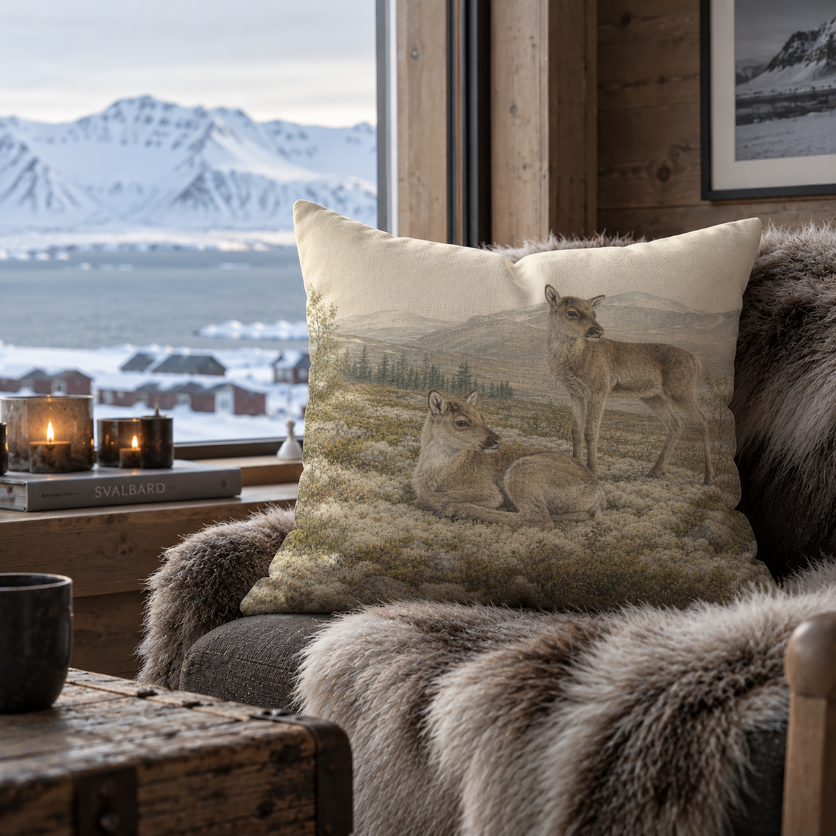 Mountain wildlife pillow cover with resting and standing reindeer calves, distant mountains and natural tundra landscape, displayed in a rustic Scandinavian home interior.